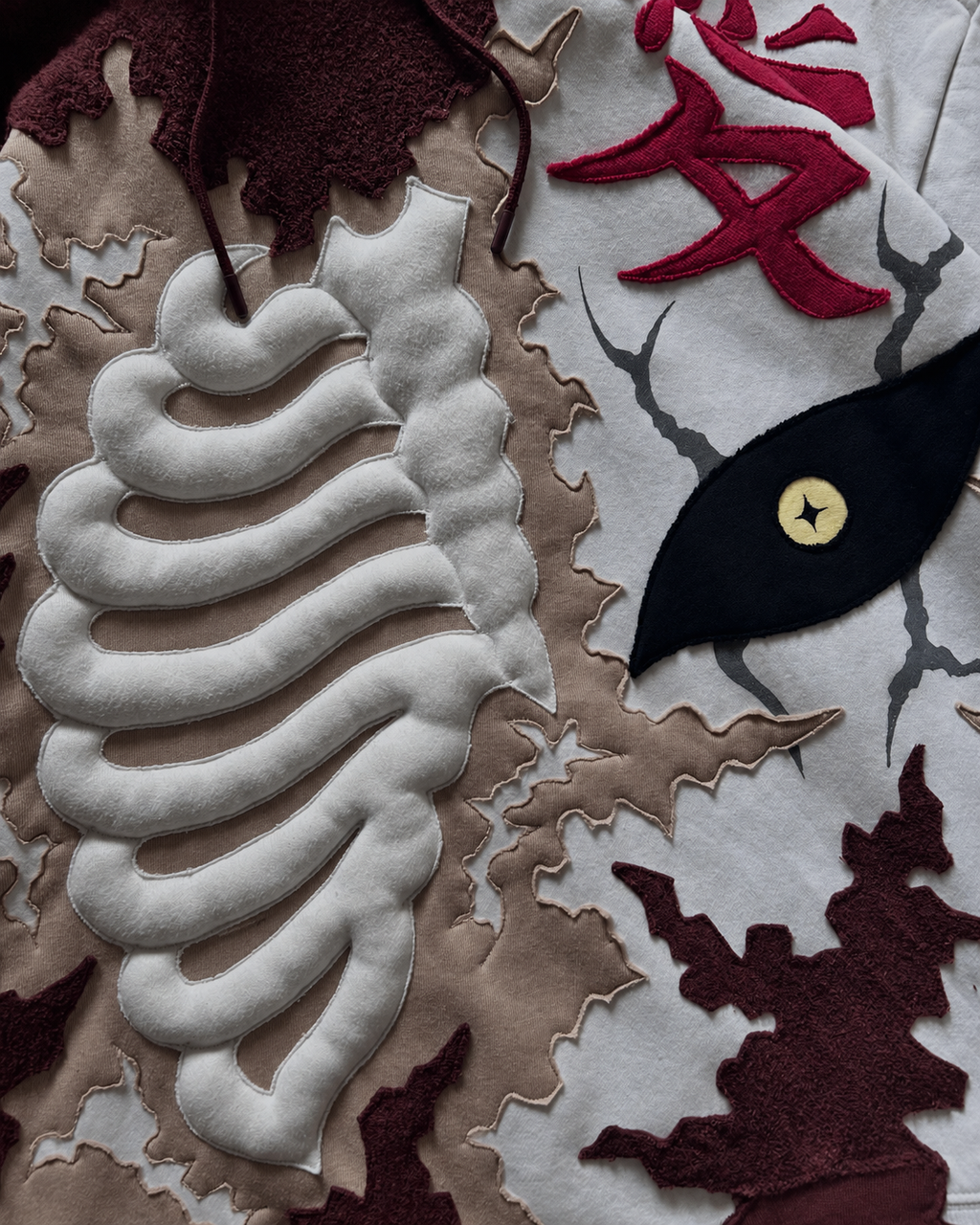 Close-up of Noctra Ivory Rift Hoodie featuring layered appliqué, embroidery and 3D skeletal detailing